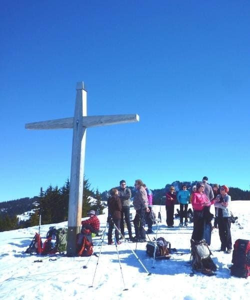 Gruppe an einem Gipfelkreuz im Schnee - Alpen