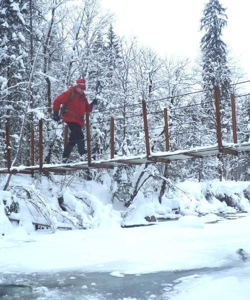 © Raymond Chabanier Wanderer überquert eine verschneite Brücke über die Subersach - Vorarlberg - Österreich