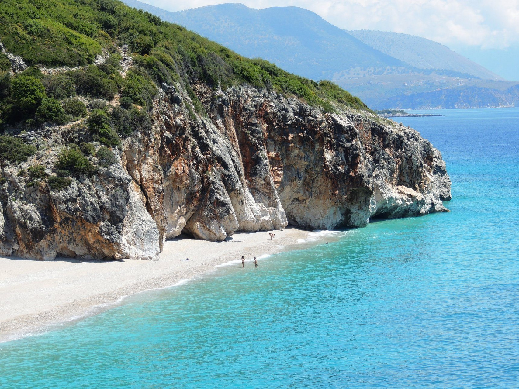 Strand mit weißem Sand, türkisfarbenem Wasser und Felsen, die ins Meer ragen